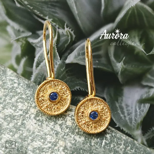 Τα Blue Orbit Earrings είναι ένα εκλεπτυσμένο κόσμημα που αποπνέει διαχρονική κομψότητα και σύγχρονη αισθητική. Κατασκευασμένα από ασήμι 925 και επιχρυσωμένα με λαμπερή, ζεστή απόχρωση χρυσού, διαθέτουν λεπτεπίλεπτο γαντζάκι που αγκαλιάζει απαλά το αυτί, χαρίζοντας άνεση και αριστοκρατική κίνηση. Ο στρογγυλός δίσκος των 9mm με τη διακριτική, ανάγλυφη υφή δημιουργεί ένα παιχνίδι φωτός που αναδεικνύει τη βαθιά μπλε πέτρα στο κέντρο — μια «τροχιά» χρώματος που μαγνητίζει το βλέμμα. Η αντίθεση του χρυσού με το έντονο μπλε προσδίδει χαρακτήρα και φινέτσα, καθιστώντας τα ιδανικά τόσο για καθημερινές εμφανίσεις με στιλ όσο και για πιο ιδιαίτερες περιστάσεις. Ένα κόσμημα που ισορροπεί ανάμεσα στη διακριτικότητα και την πολυτέλεια — μια μικρή, φωτεινή λεπτομέρεια που ολοκληρώνει κάθε σύνολο με αέρα υψηλής αισθητικής. Χαρακτηριστικά: Υλικό: Ασήμι 925 Φινίρισμα: Επιχρυσωμένο Διάμετρος δίσκου: 9mm Πέτρα: Μπλε Κούμπωμα: Γαντζάκι