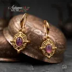 Ατσάλινα κρεμαστά σκουλαρίκια Theodora Earrings σε χρυσό χρώμα, με οβάλ μωβ αμέθυστο και περίτεχνο διάτρητο πλαίσιο